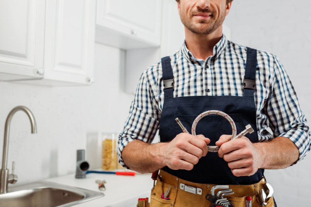 A man in blue overalls stands confidently, holding a wrench in his right hand, ready for mechanical work.