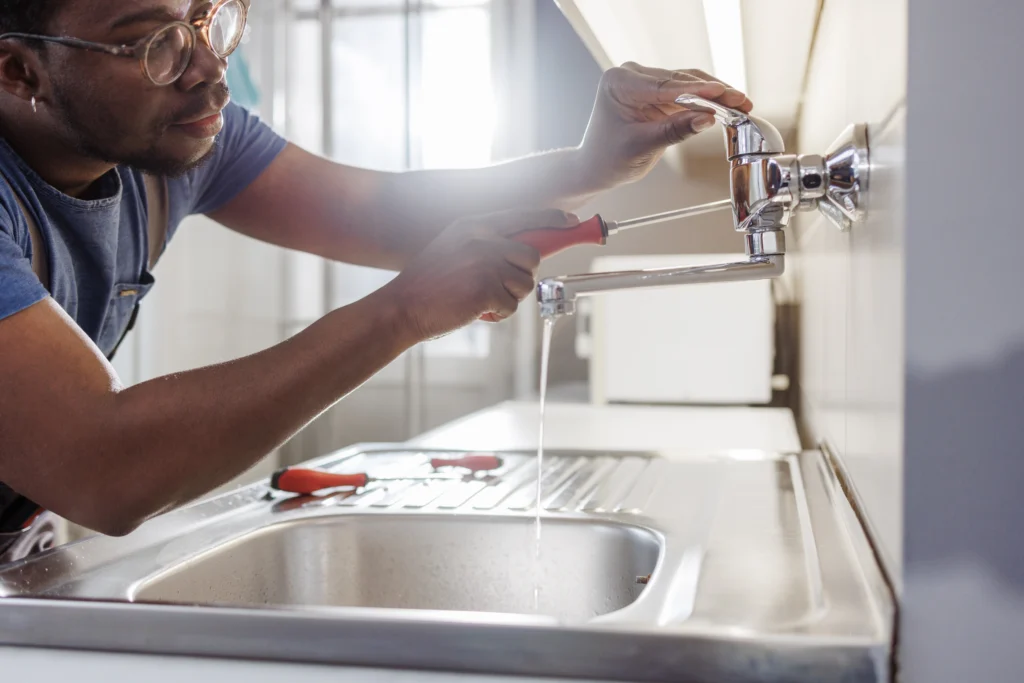 A man wearing glasses is repairing a sink faucet, demonstrating his plumbing skills and attention to detail.